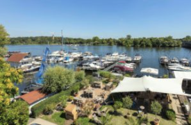 Blick auf einen Yachthafen mit vielen Booten an einem sonnigen Tag und eine Terrasse mit Sitzgelegenheiten im Freien.