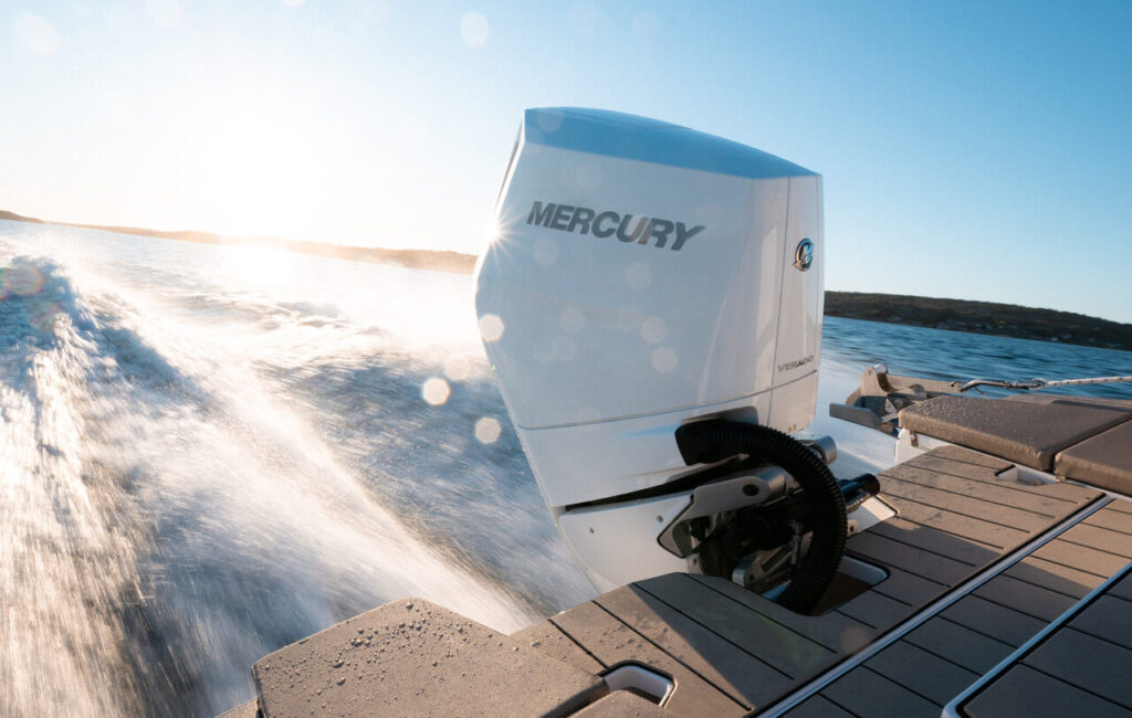 Ein weißer Mercury Außenbordmotor an einem fahrenden Boot, das bei hellem Sonnenschein eine Gischt auf dem Wasser erzeugt.